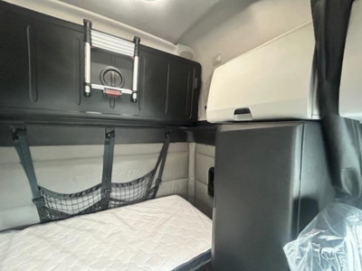 Interior of a 2022 Freightliner Cascadia 126 sleeper cab showing upper storage cabinet, window shade, and sleeper netting over a mattress.