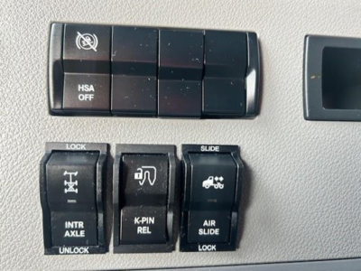Cab interior panel showing switch blocks labeled HSA OFF, LOCK, SLIDE, INTR AXLE, K-PIN REL, AIR SLIDE LOCK, with icons.