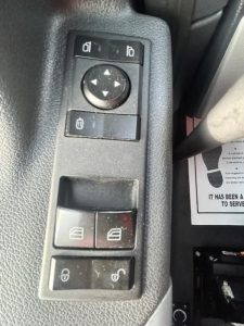 Truck interior switch panel with window controls and mirror adjustment on Freightliner Cascadia dash. Visible: circular joystick, two top small buttons, two middle window switch blocks, bottom lock switches.