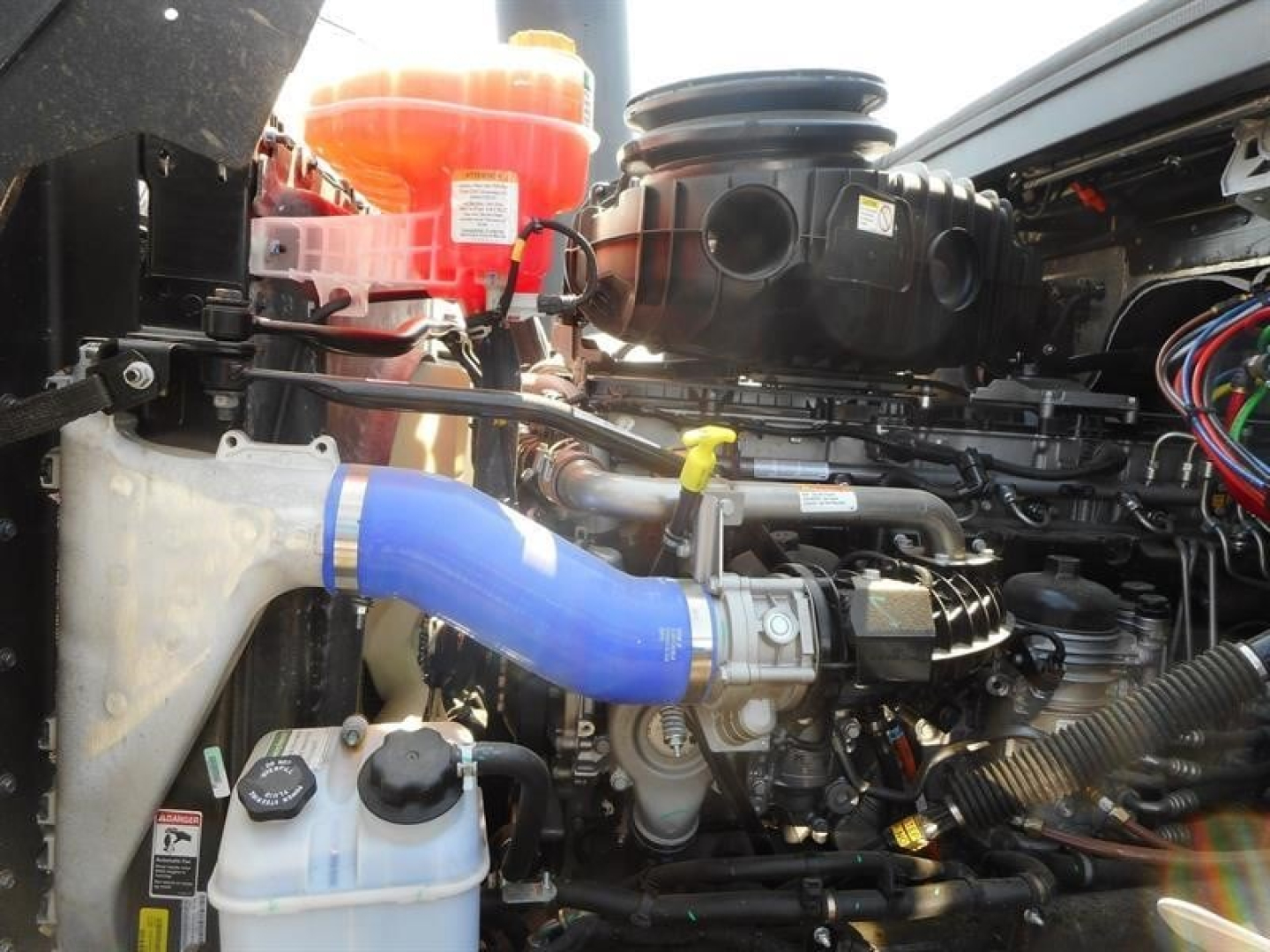 Engine bay of a 2027 Western Star 49X showing blue intercooler hose, coolant reservoir, wiring harness, and various engine components.