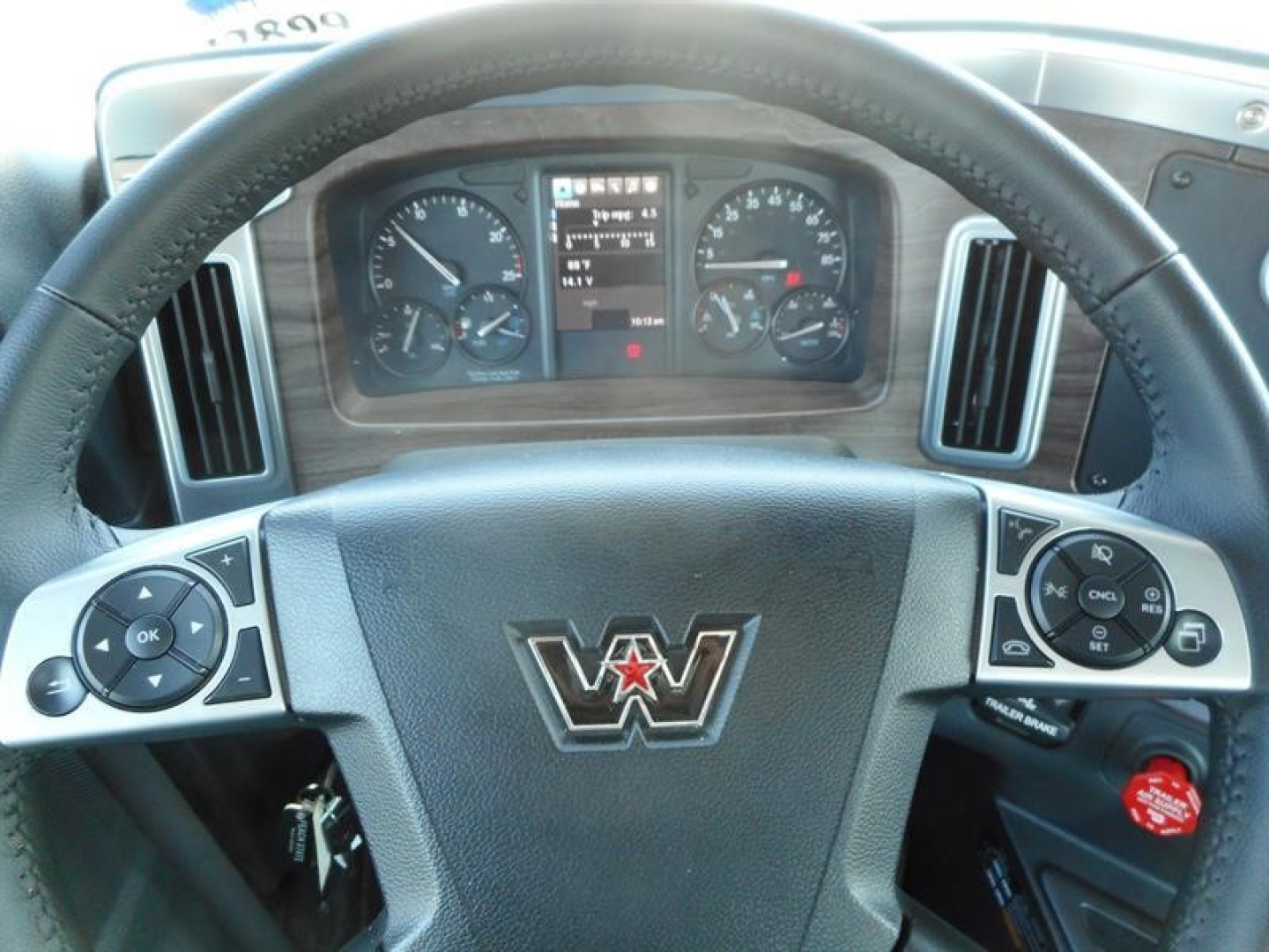 Steering wheel and instrument cluster of a 2027 Western Star 49X truck cab showing dashboard gauges and control buttons on the steering wheel.