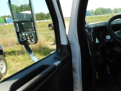Vehicle cab interior view with door panel and mirror, showing part of dashboard and steering wheel.