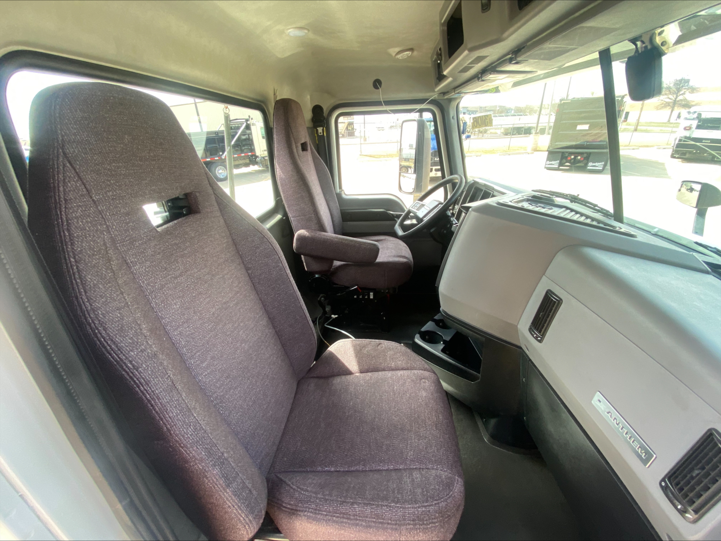 Truck cab interior of a 2021 Mack AN42T showing driver seat, passenger seat, dashboard, and steering wheel with fabric seats.