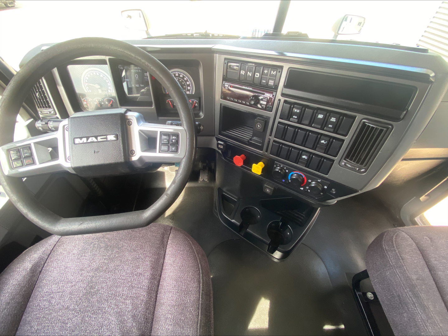 Dashboard and steering wheel of a 2021 Mack AN42T daycab truck interior with steering wheel, gauges, and center console controls.