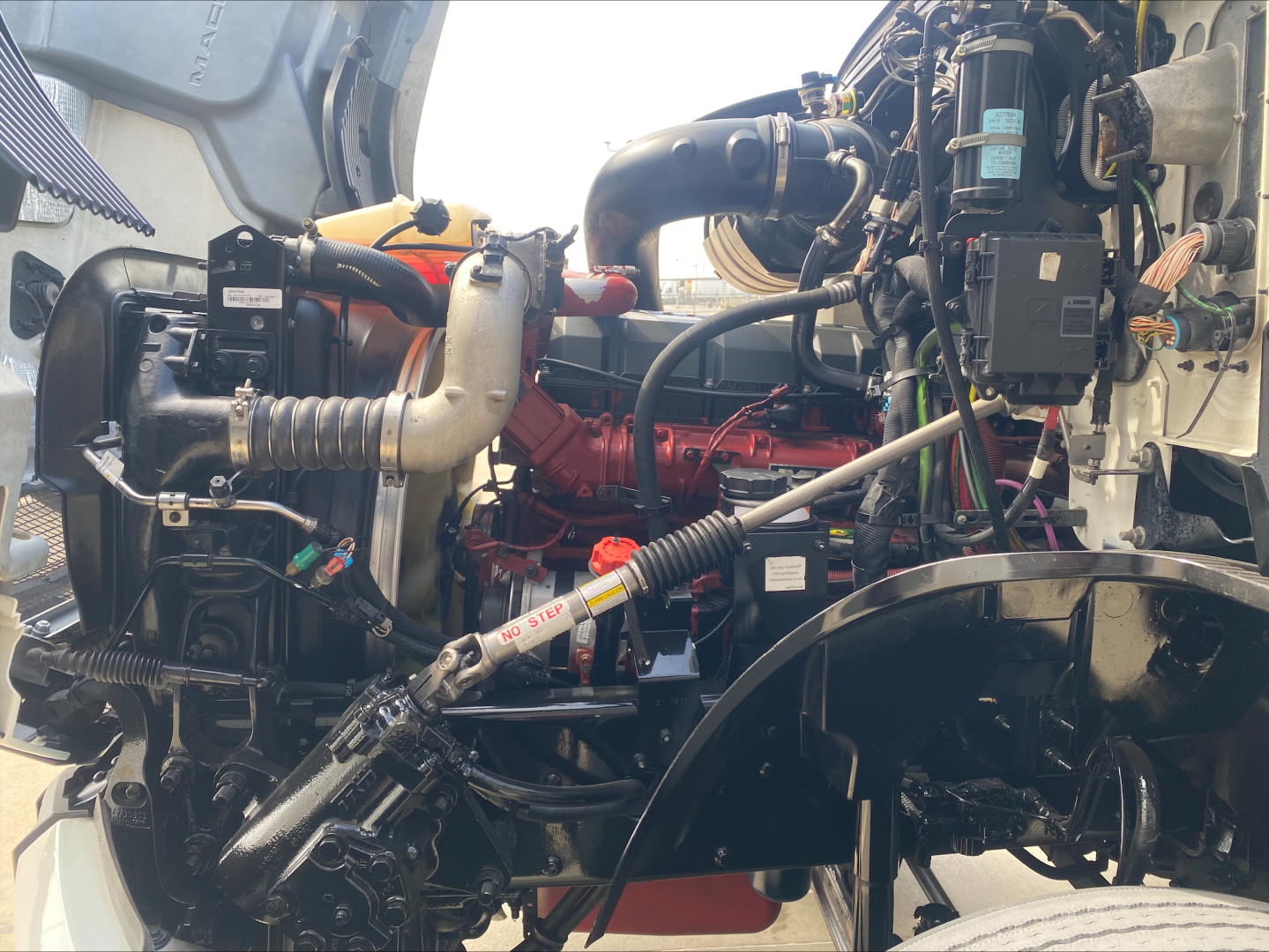 Engine bay of 2021 Mack AN42T showing large red engine, intake tubing, hoses, and various components in view.