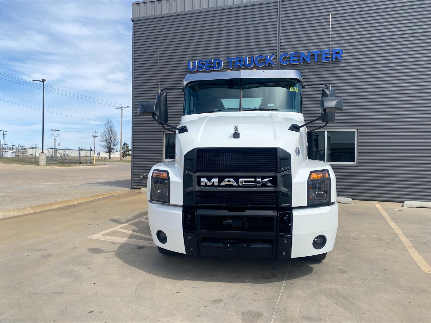 Front view of a white 2021 Mack AN42T conventional daycab truck parked in a lot in front of a used truck center building.