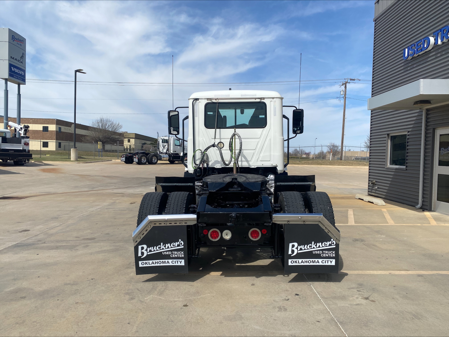 Rear view of a white 2021 Mack AN42T daycab truck in a dealership lot, showing dual rear mud flaps with Bruckner's Oklahoma City branding and chassis details.