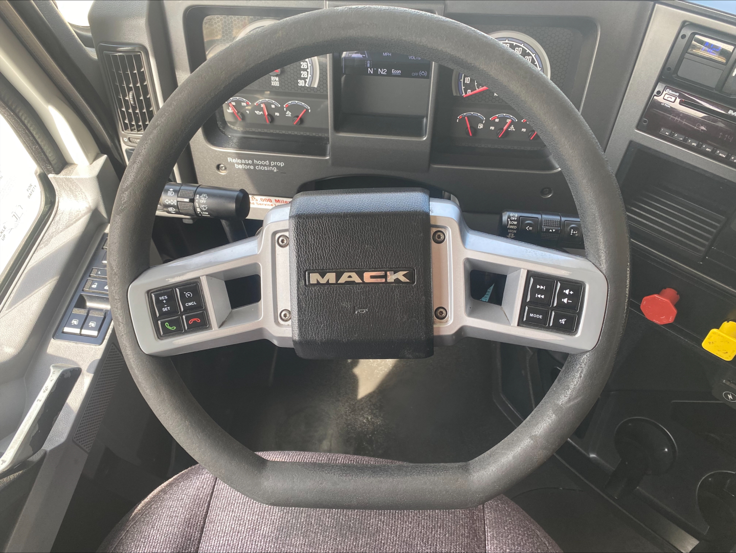 Steering wheel center with MACK logo inside truck cab dashboard showing gauges and controls.