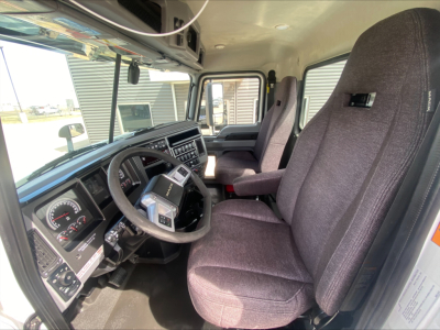 Interior of a 2021 Mack AN42T truck cabin, showing steering wheel, dashboard gauges, driver and passenger seats, and front door area.