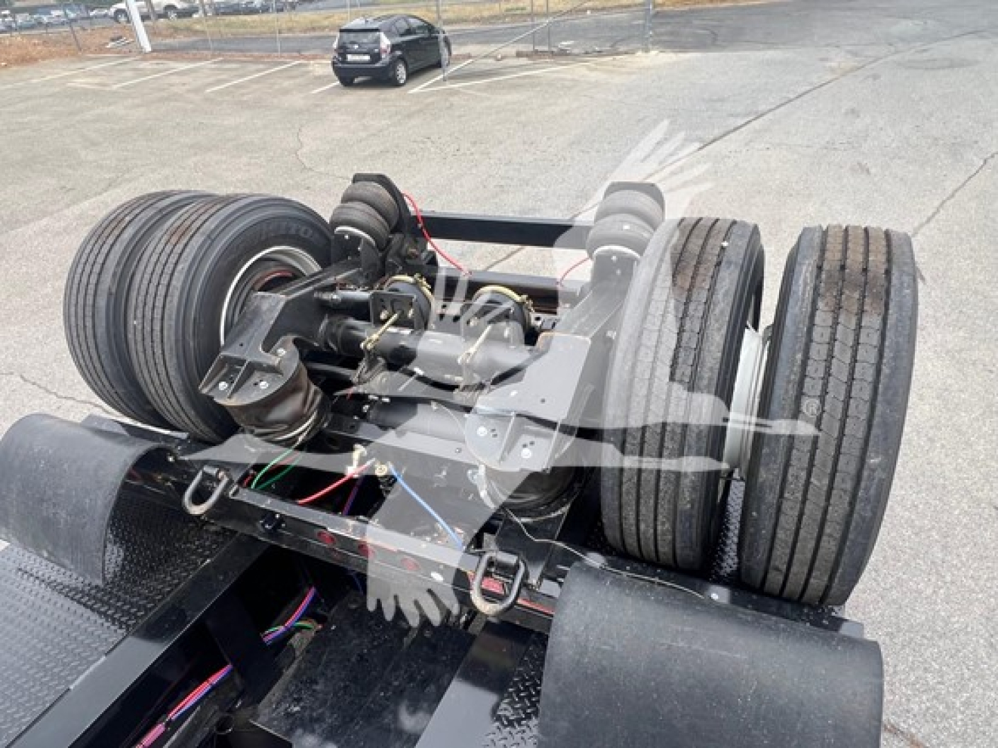 Trailer flip axle with dual rear axles and heavy-duty suspension, visible tires and mounting components, warehouse lot background.