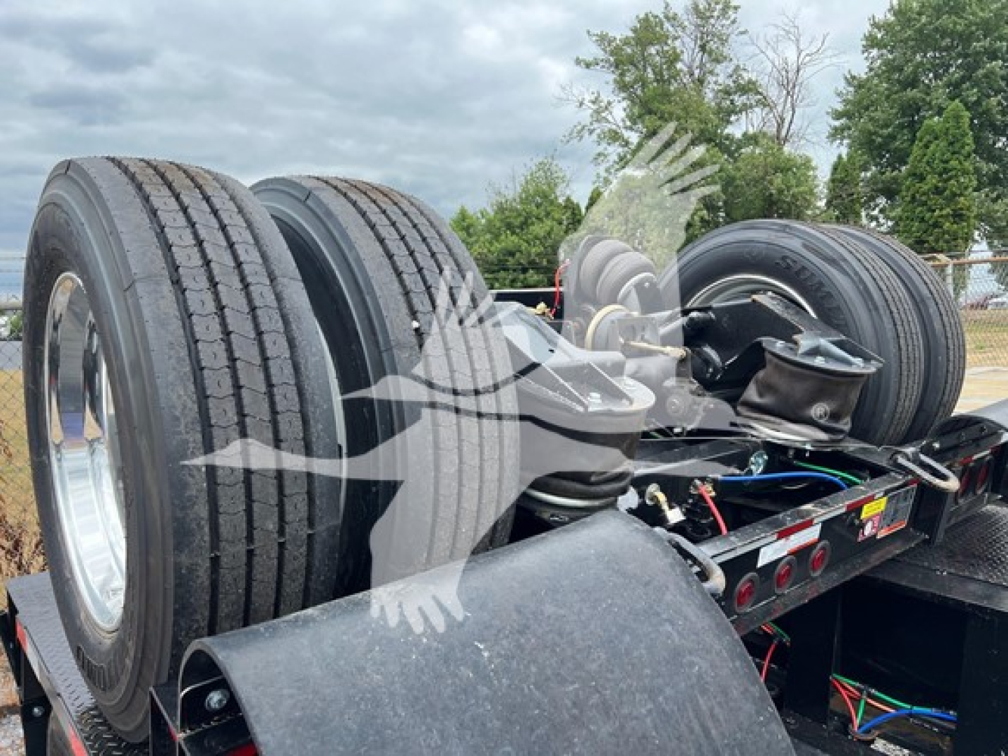 Trailer showing dual rear axles with large tires and wiring harnesses; lowboy trailer chassis visible with hydraulic components and wheel hubs.