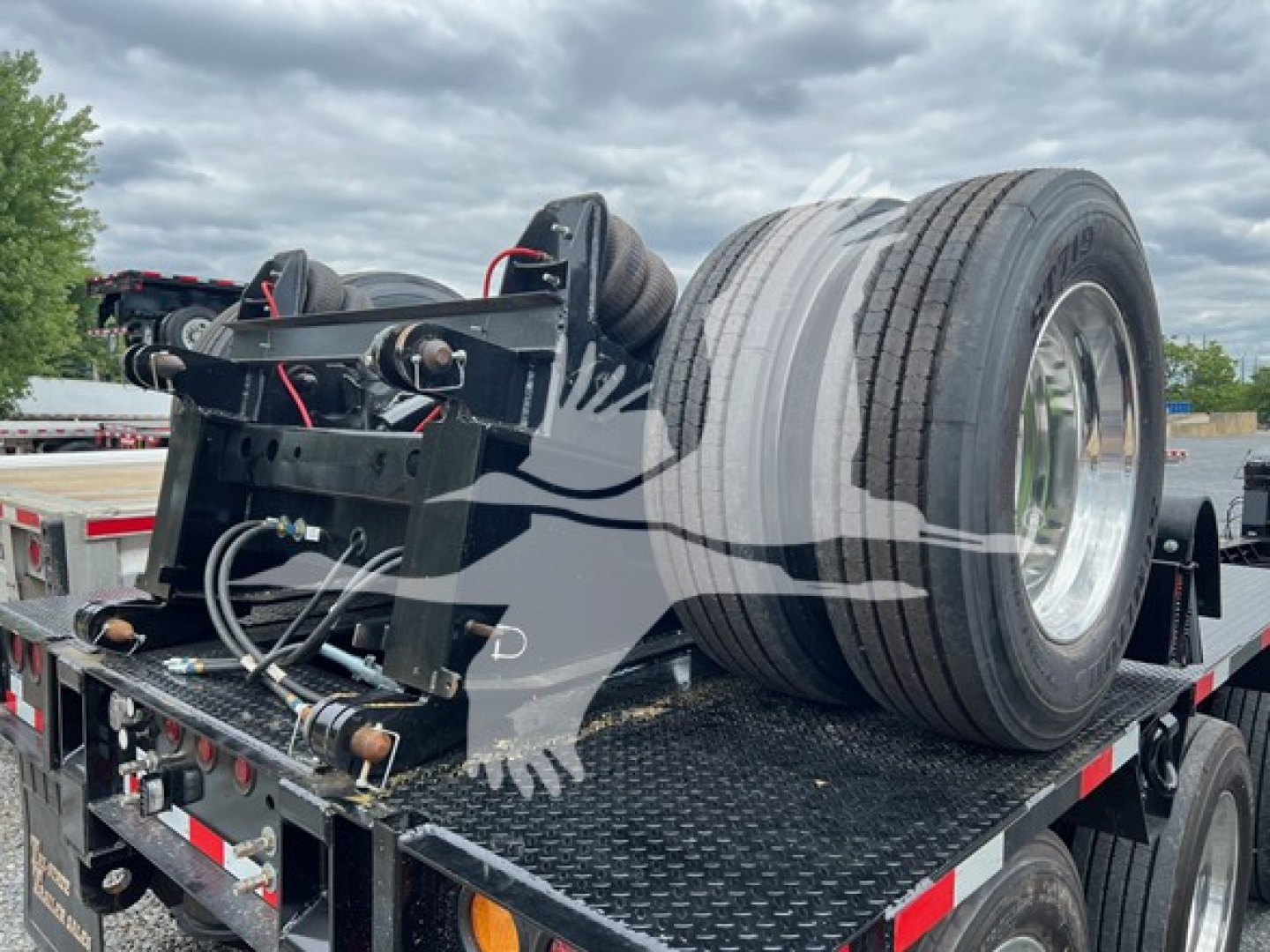 Trailer component showing flip axle assembly mounted on a lowboy trailer bed with dual tires and hydraulic lines visible