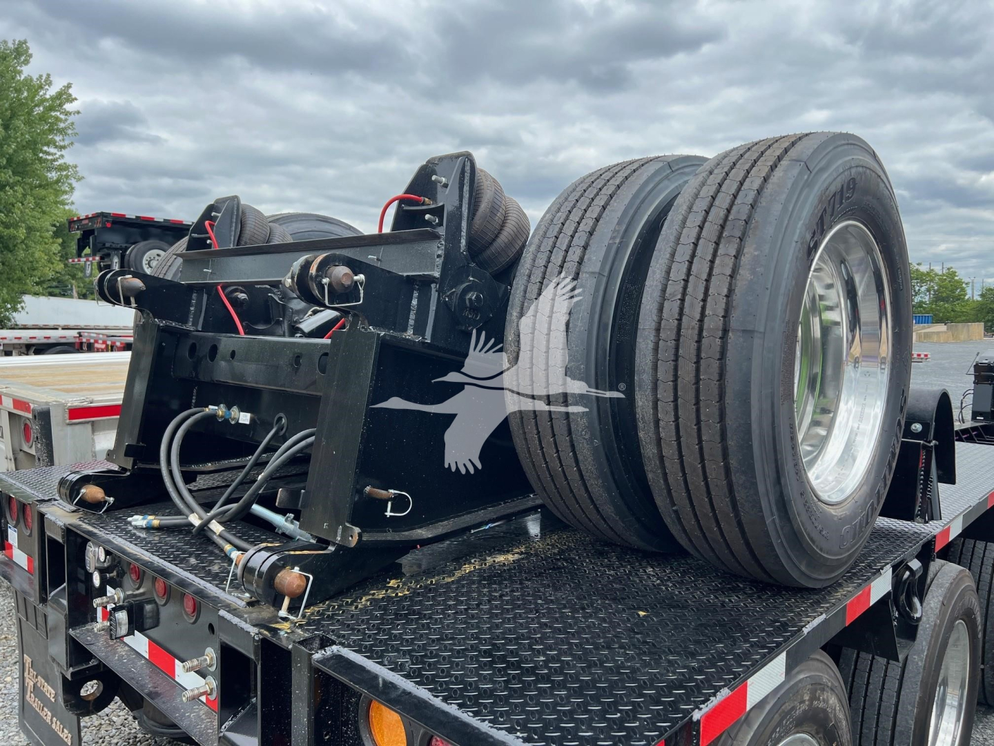 Trailer axle assembly mounted on a lowboy trailer with dual wheels and hydraulic components visible.