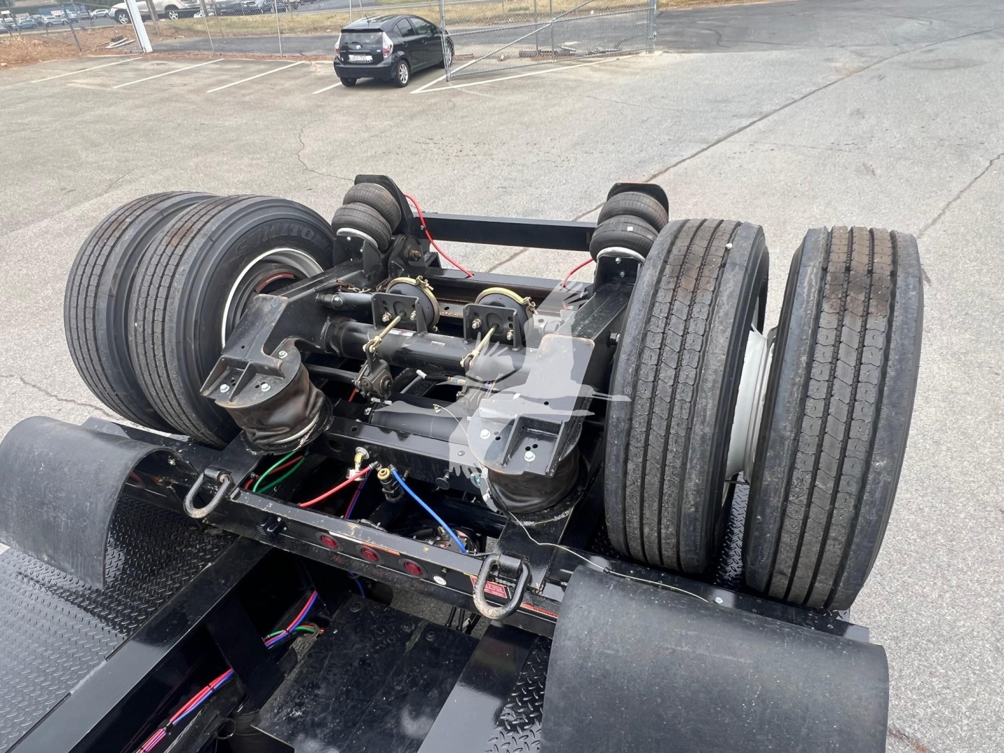 Trailer tandem axle assembly with dual sets of air springs, hoses, and electrical lines visible; large dual tires on each side.