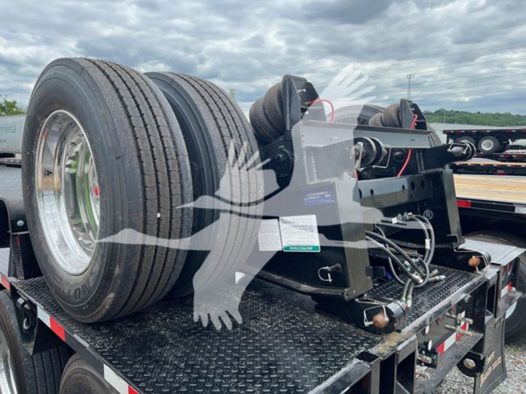 Trailer shows dual axle flip axle assembly on flatbed with tires and mounting brackets. Visible labels and components on the platform.