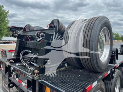 Trailer component showing flip axle assembly mounted on a lowboy trailer bed with dual tires and hydraulic lines visible