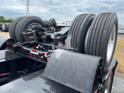 Dual rear axle of a lowboy trailer with large tires and landing gear, side rails, and suspension components visible.