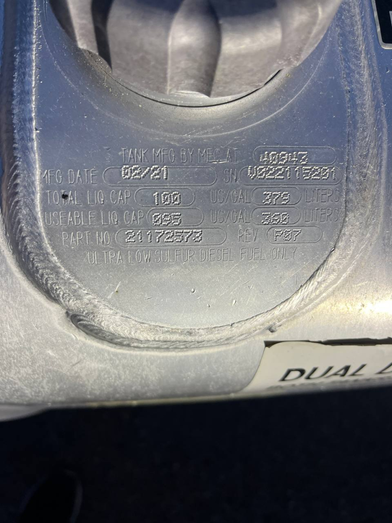 Engine bay label showing tank info: MFG DATE 02/21, TOT. LNG CAP 150D, MFG 2021? plus serial numbers and DEF label. Circular cap area with embossed text.