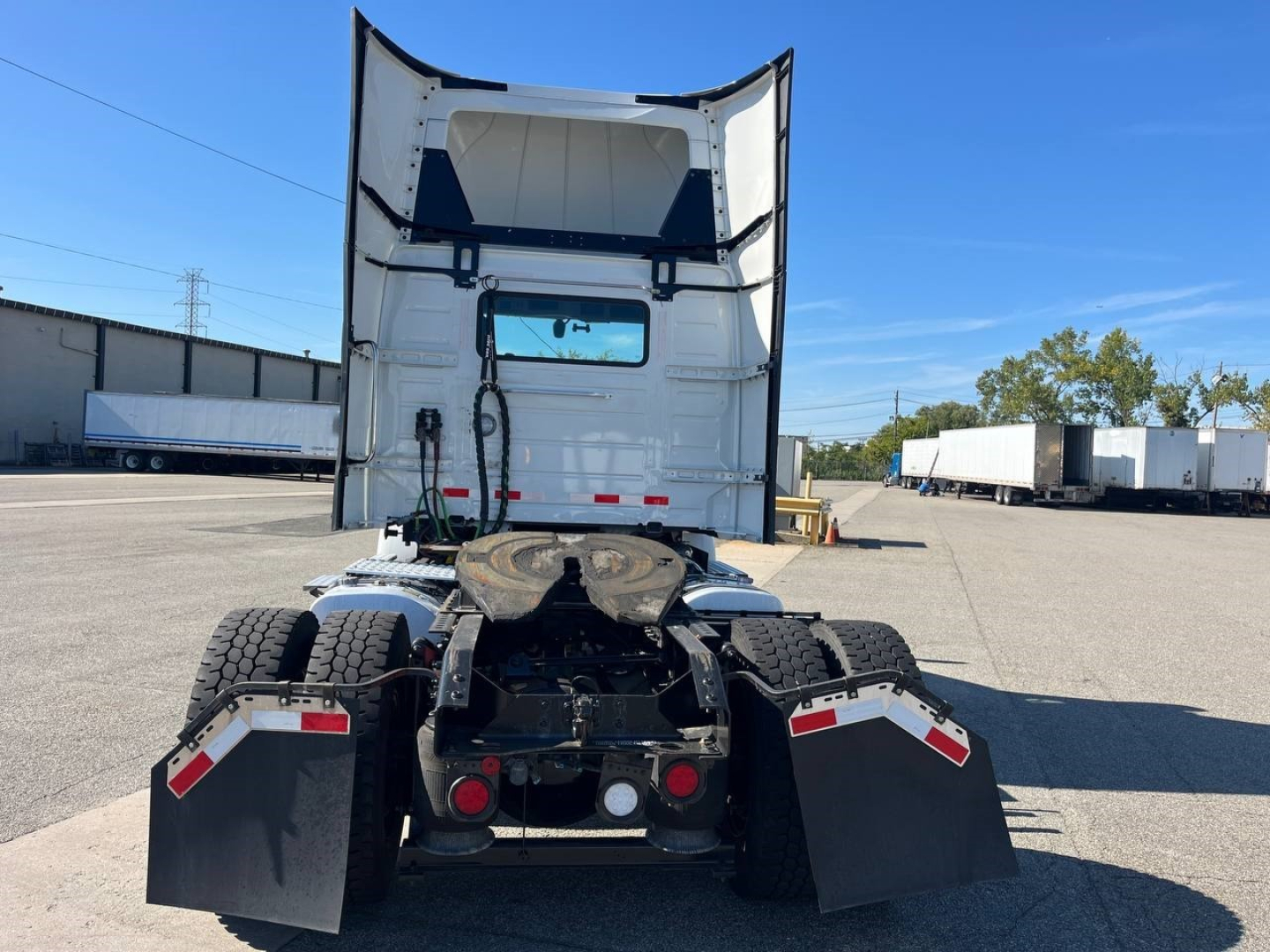 Rear view of a 2022 Volvo VNR300 4x2 day cab tractor showing dual rear axles, mud flaps, and chassis with fifth wheel and cab roof opened.