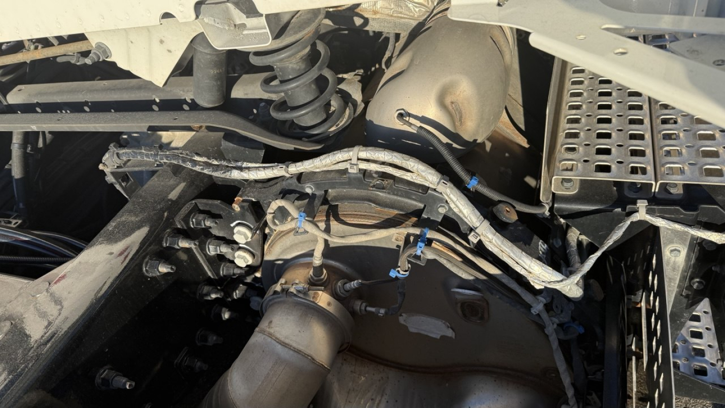 Volvo VNR300 engine bay showing wiring harnesses and exhaust system components in a day cab truck, view from side.