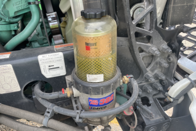 Engine bay showing hydraulic or fuel filter canister labeled 'Fuel 3B' with Dagvosmart? surrounding hoses and a yellow translucent reservoir