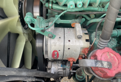 Volvo engine bay showing belt-driven alternator and surrounding green engine components in a day cab truck.