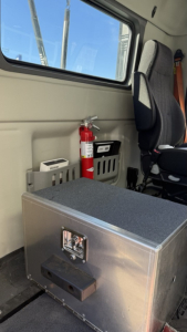 Vehicle interior showing a metal toolbox with latch, fire extinguisher, and seat in a Volvo VNR300 day cab unit compartment.
