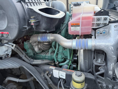 Volvo VNR300 engine bay showing coolant reservoir and intake tubing with blue silicone hoses and various engine components.