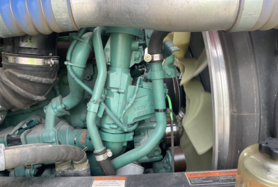Volvo engine bay showing green Volvo engine with hoses and belts in a day cab truck.