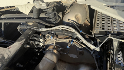 Volvo VNR300 engine bay showing wiring harnesses and exhaust system components in a day cab truck, view from side.