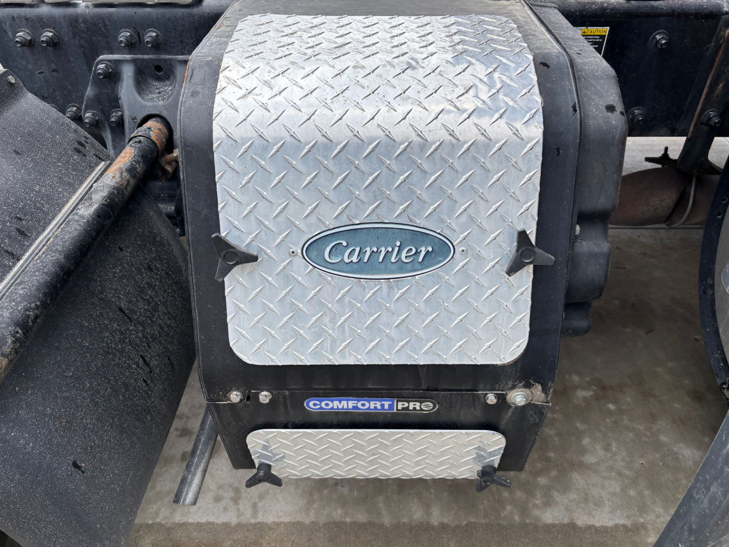 Carrier air conditioning unit mounted under Kenworth T680 with diamond plate cover and ComfortPro label.