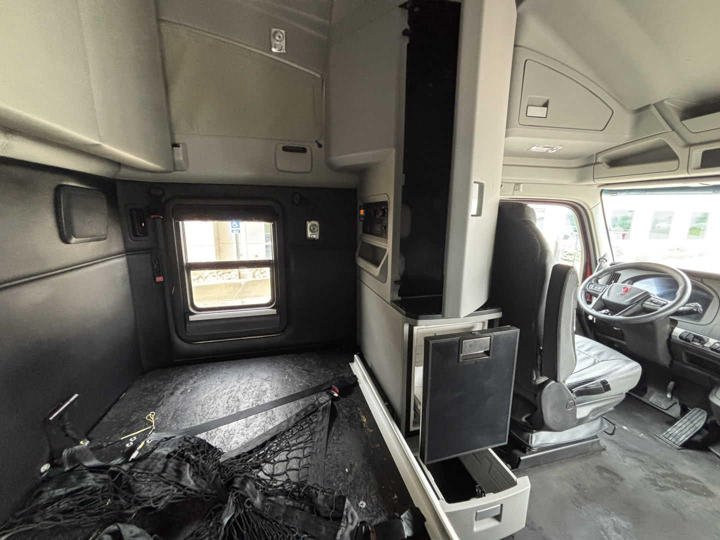 Truck cab interior with sleeper area and driver's seat visible; storage compartments and control panels along the side.