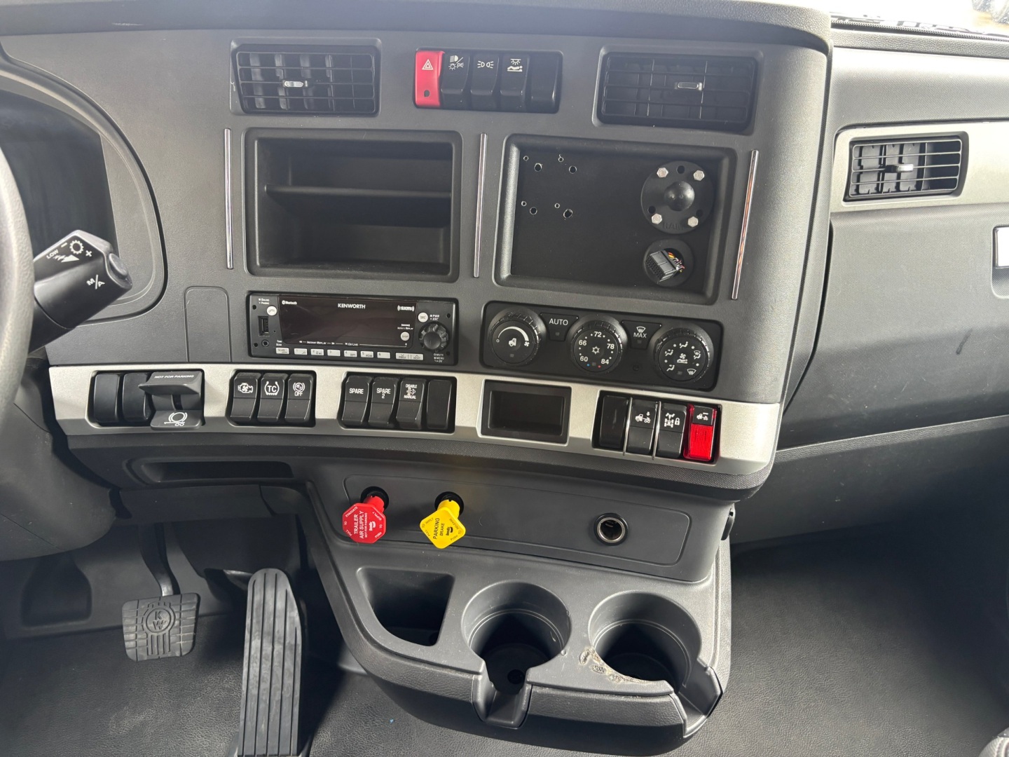 Dashboard interior of a 2023 Kenworth T680 showing switches, vents, cup holders, and control panels.