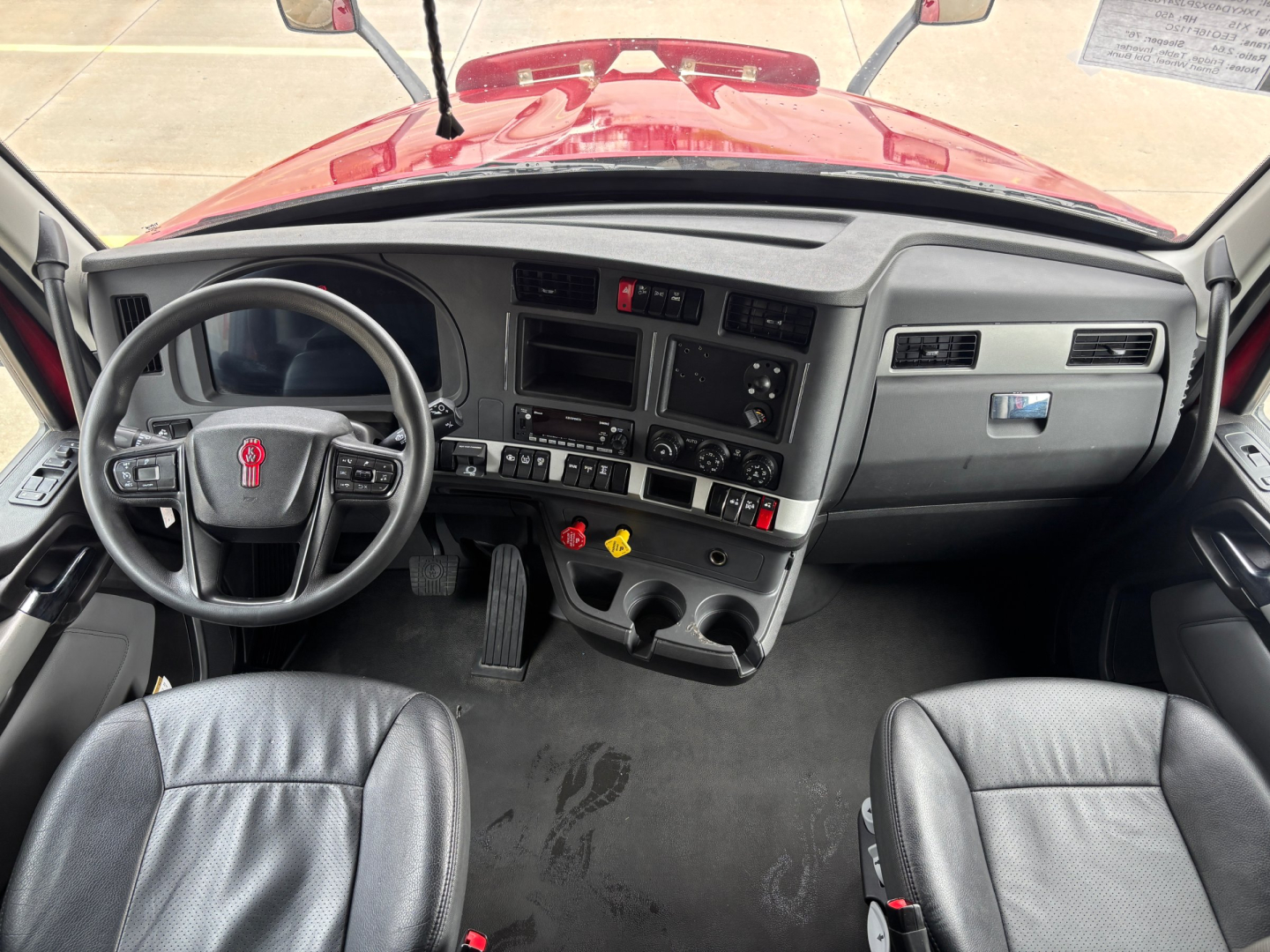 Kenworth T680 dashboard and driver seat view showing steering wheel, instrument cluster, center console, and dual cup holders.
