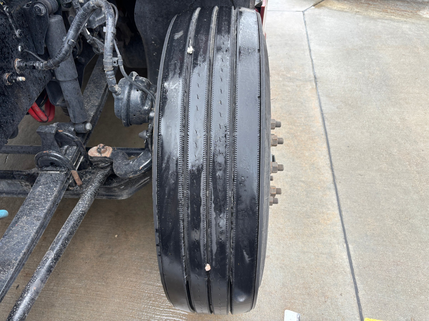 Kenworth T680 truck front axle area with triple-dip belt and components visible; close-up of large aluminum drum brake or wheel hub with bolts on the side.