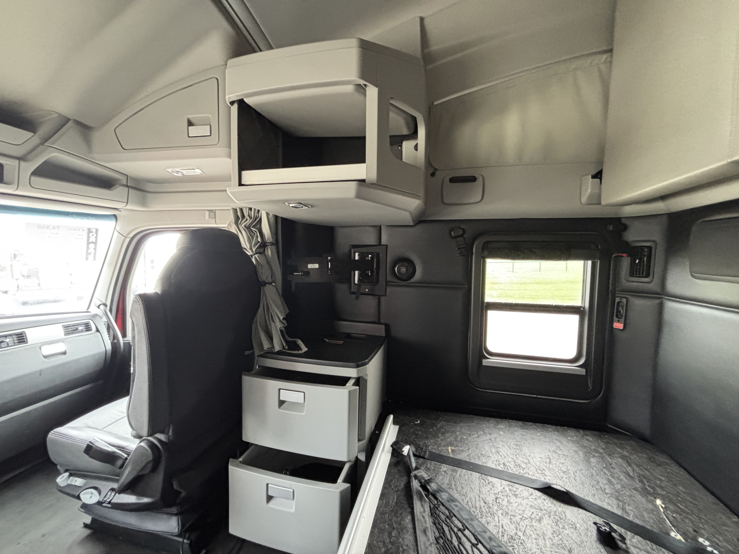 Interior of a Kenworth T680 truck cab showing overhead storage shelf and cabin drawer units with gray panels and a small window.