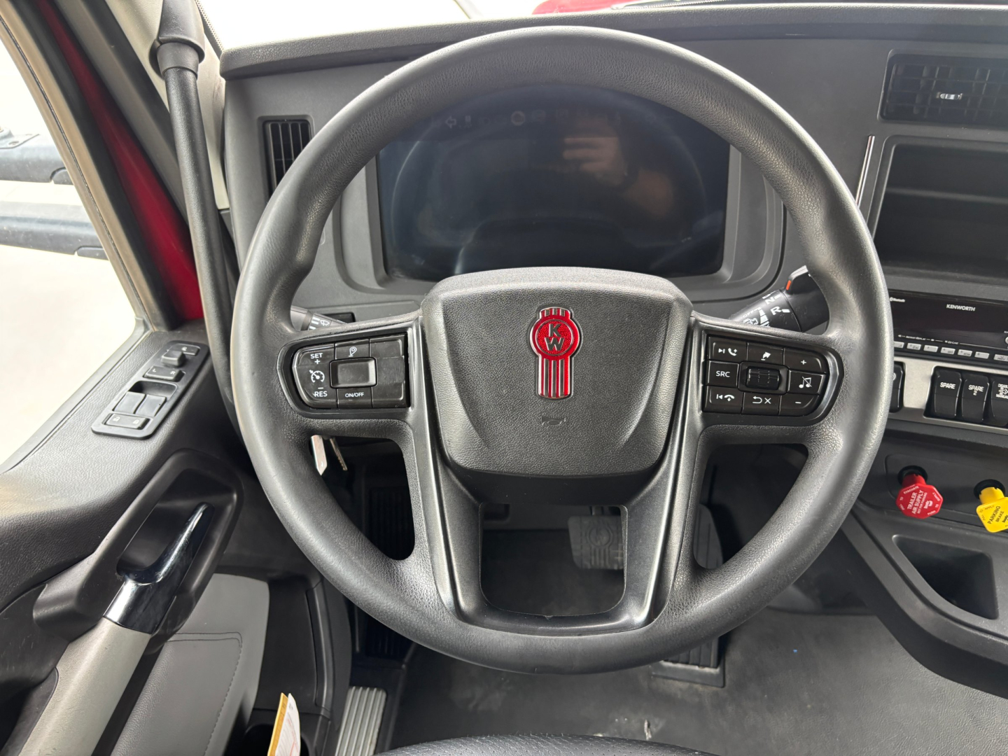 Steering wheel of a 2023 Kenworth T680 cab interior with Kenworth logo and integrated controls, dashboard screen visible.