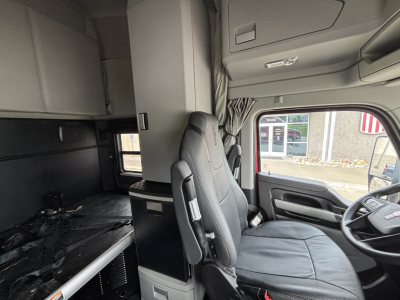Kenworth T680 truck cab interior view showing driver seat, dashboard, and sleeper storage area with overhead cabinets.