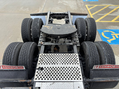 Kenworth T680 chassis exposed with dual rear axles and perforated metal step, showing wheels and suspension components.
