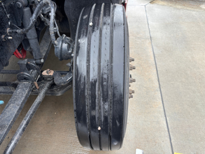 Kenworth T680 truck front axle area with triple-dip belt and components visible; close-up of large aluminum drum brake or wheel hub with bolts on the side.