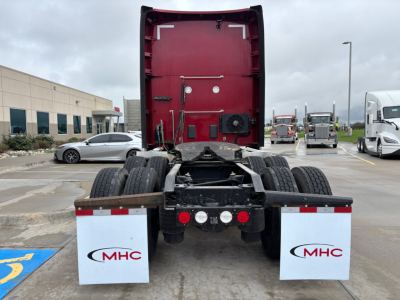 Kenworth T680 rear view showing fifth wheel area, dual rear axles, mud flaps with MHC logos, and cab with red back panel.