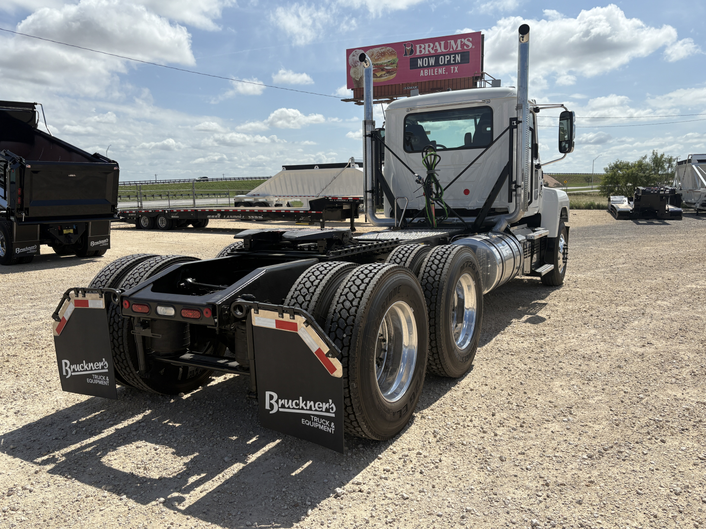 Tractor-trailer rear view showing dual rear axles and mud flaps with Bruckners Equipment logo, white cab, flatbed area, and fifth-wheel coupling.