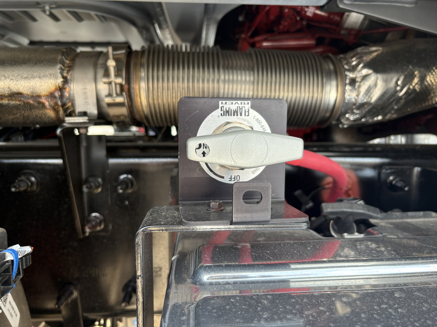 Truck engine bay of a 2027 Mack PI64T showing a fuel cap lock and nearby hoses and components.
