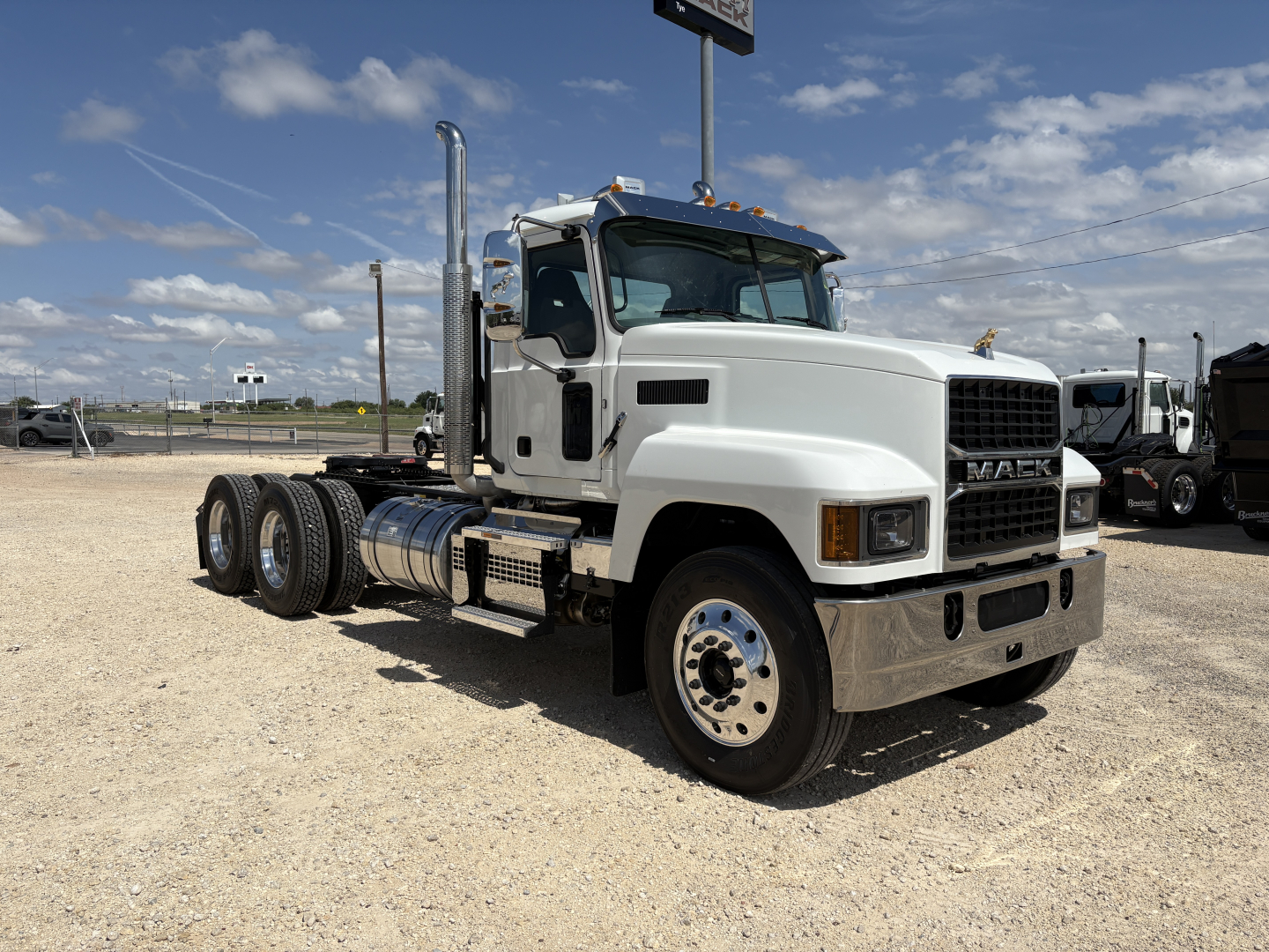 White 2027 Mack PI64T conventional daycab truck front-right view showing cab, grille, dual exhaust stacks, and six-wheel configuration.