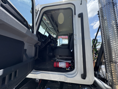 Truck cab interior of a new 2027 Mack PI64T daycab showing driver's seat and door area with a fire extinguisher on the floor.