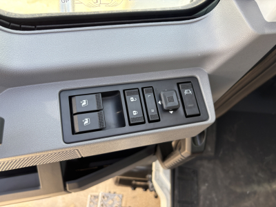 Mack PI64T truck interior controls panel showing window/lock switches and mirror adjustment; part of dashboard near driver seat.