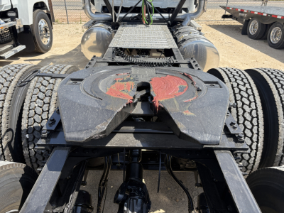 Semi truck fifth wheel and chassis showing rear view of a new Mack PI64T tractor, dual rear tandem wheels, fuel tanks, steps, and fifth wheel with red placard.