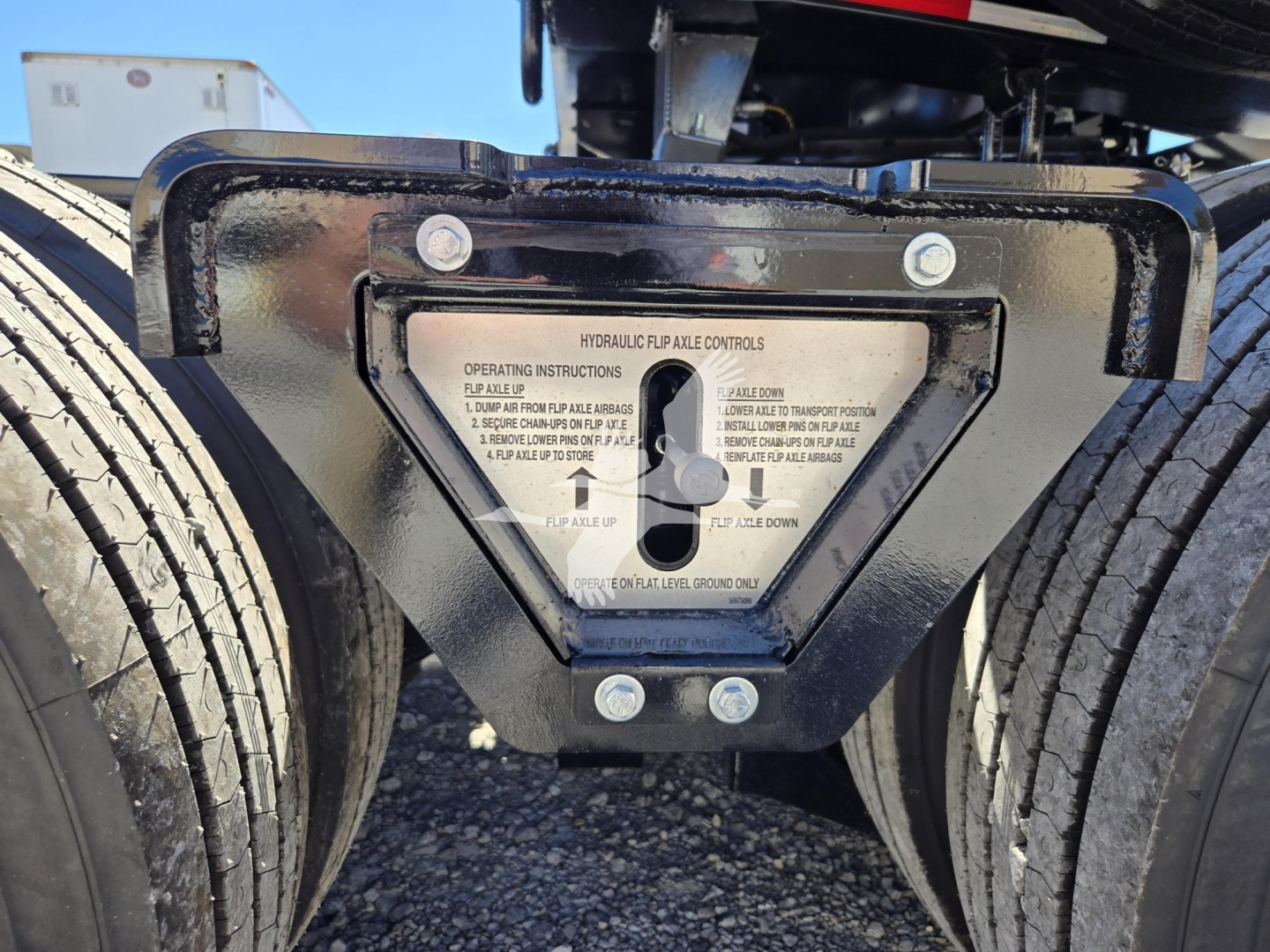 Hydraulic flip controls plate mounted between trailer axles with screws and labeled instructions.