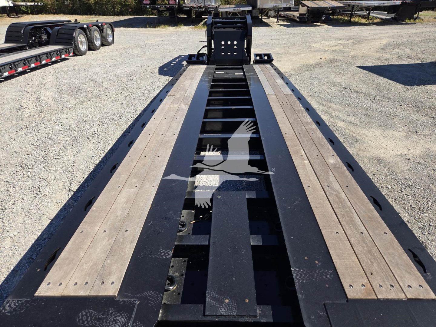 Trailer bed of a Fontaine lowboy with long wooden deck beams and hydraulic flip mechanism visible, center frame and landing gear, outdoor lot.