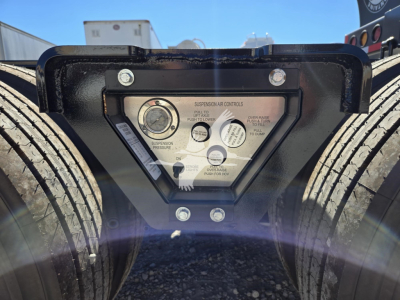Trailer chassis with hydraulic flip mechanism control panel and dual tires; close-up of suspension controls and labels on black triangular plate between wheels.